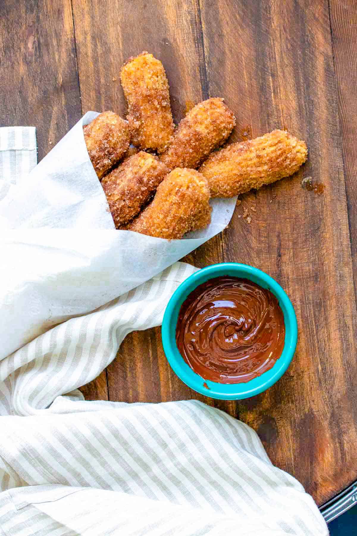 Vegan churros wrapped in a parchment cone next to a bowl of chocolate.