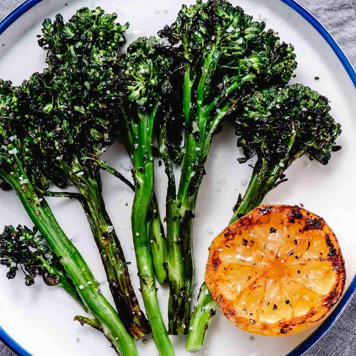 grilled baby broccoli with lemon on white plate.