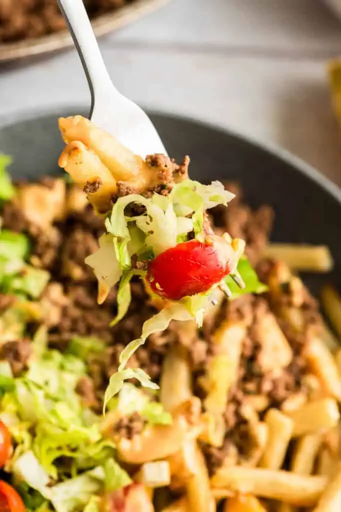Forkful of fries, ground beef, lettuce and tomato.