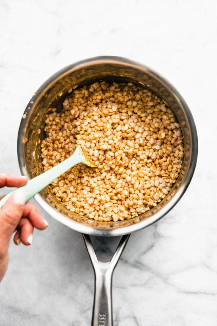 2. Crispy rice cereal being stirred into a warm maple and nut butter mixture in a saucepan.