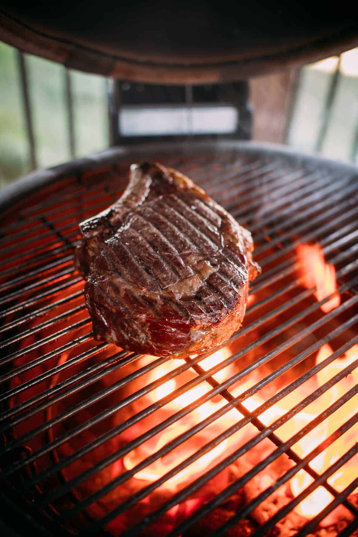 A thick cut steak is being seared over open flames on a barbecue grill.