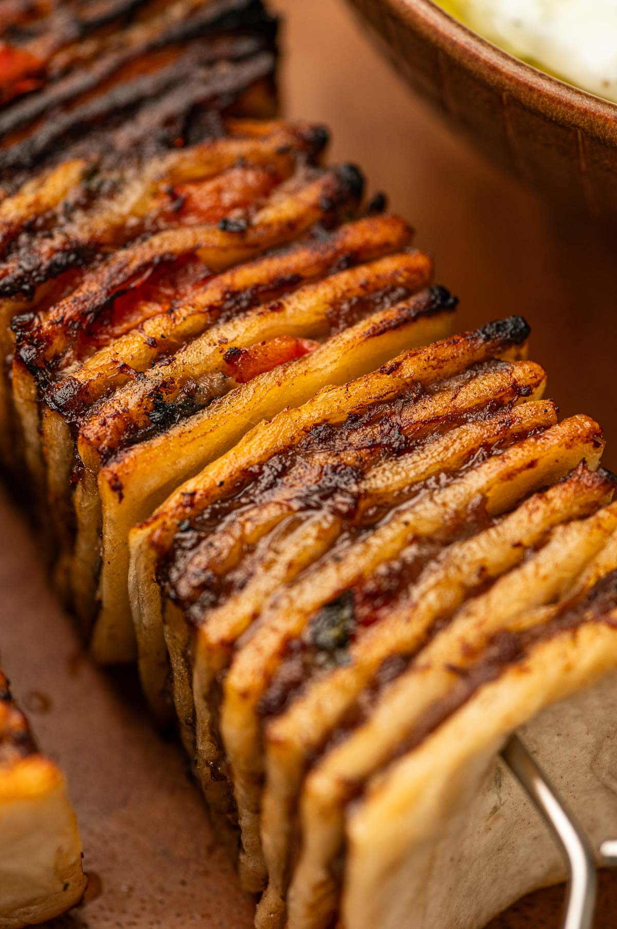 Close-up of stacked tortillas filled with cooked ground lamb layered onto a skewer with charred golden brown edges from the grill.