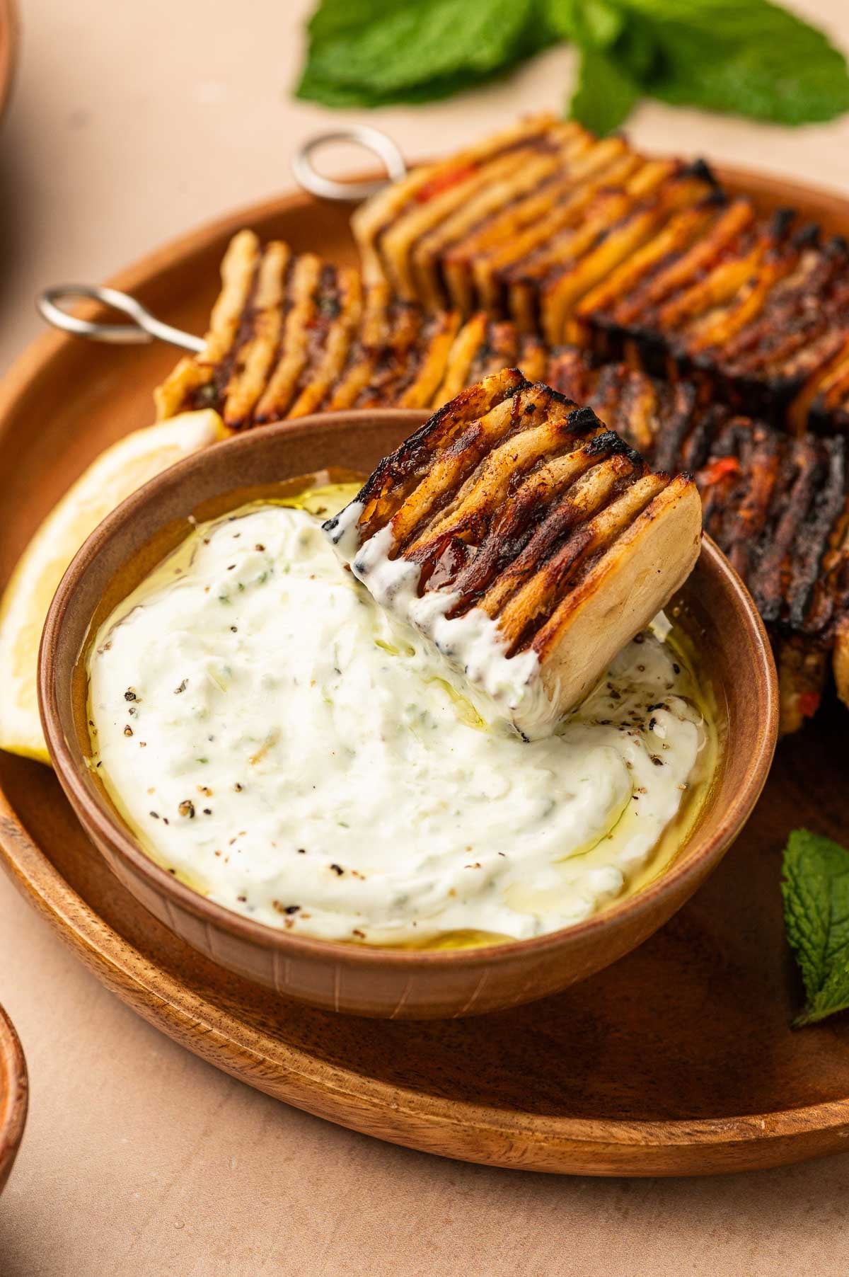 Grilled tortilla kebobs are served on a plate with a side of creamy yogurt dip, with one skewer being dipped into the sauce.