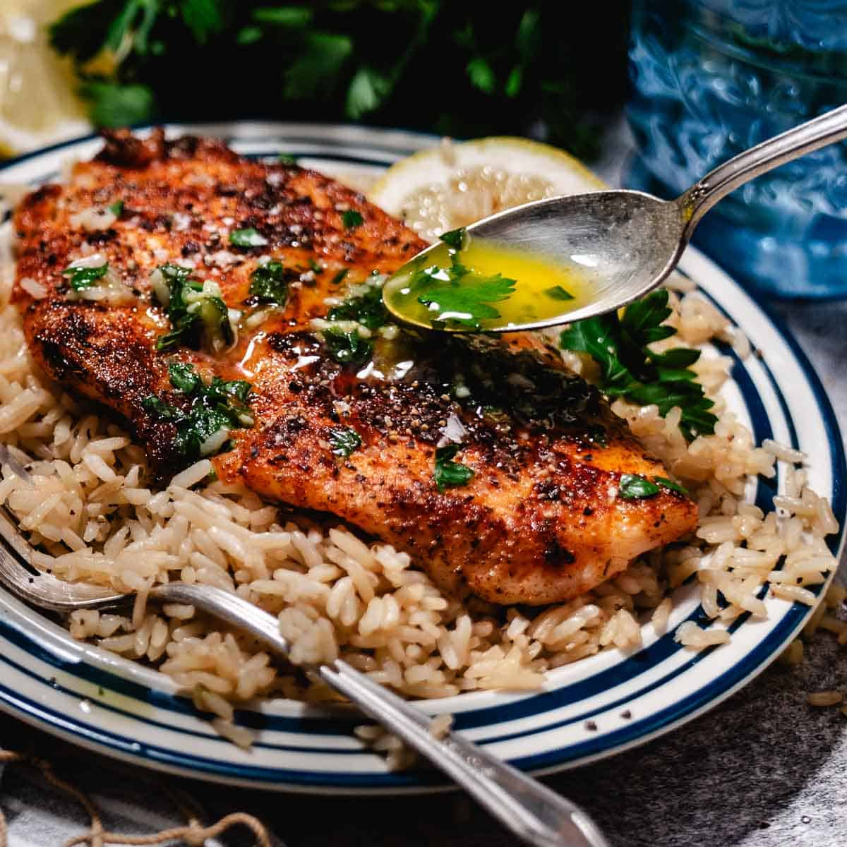 A golden fillet of fish topped with rich lemon garlic butter sauce and fresh herbs.
