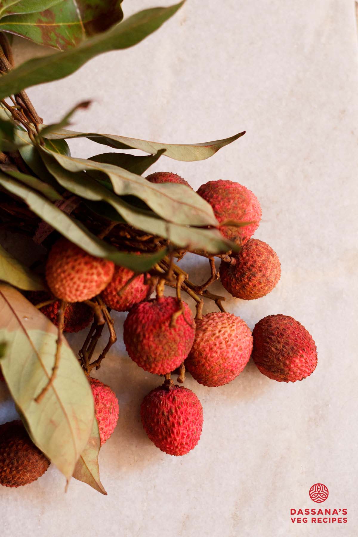 Fresh lychee fruit with leaves on a marble table.