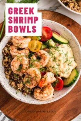 Greek shrimp bowls filled with shrimp, quinoa, cucumber tomato salad on a wood plate.