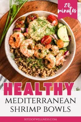 Greek shrimp bowls filled with shrimp, quinoa, cucumber tomato salad on a wood plate.