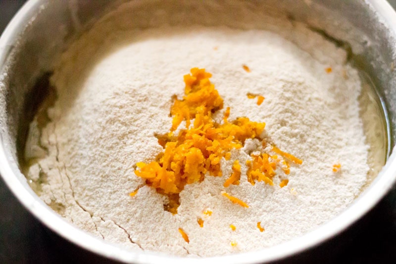 Orange zest added to sifted dry ingredients in bowl.