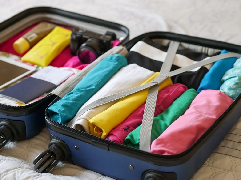 Open suitcase packed with folded clothes, sunglasses and a camera