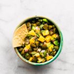 Small bowl of pickle and mango salsa topped with a tortilla chip on the side.