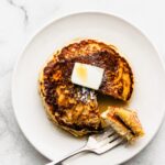 Gluten-free pancakes on a white plate topped with butter and syrup, with a fork holding a cut piece.