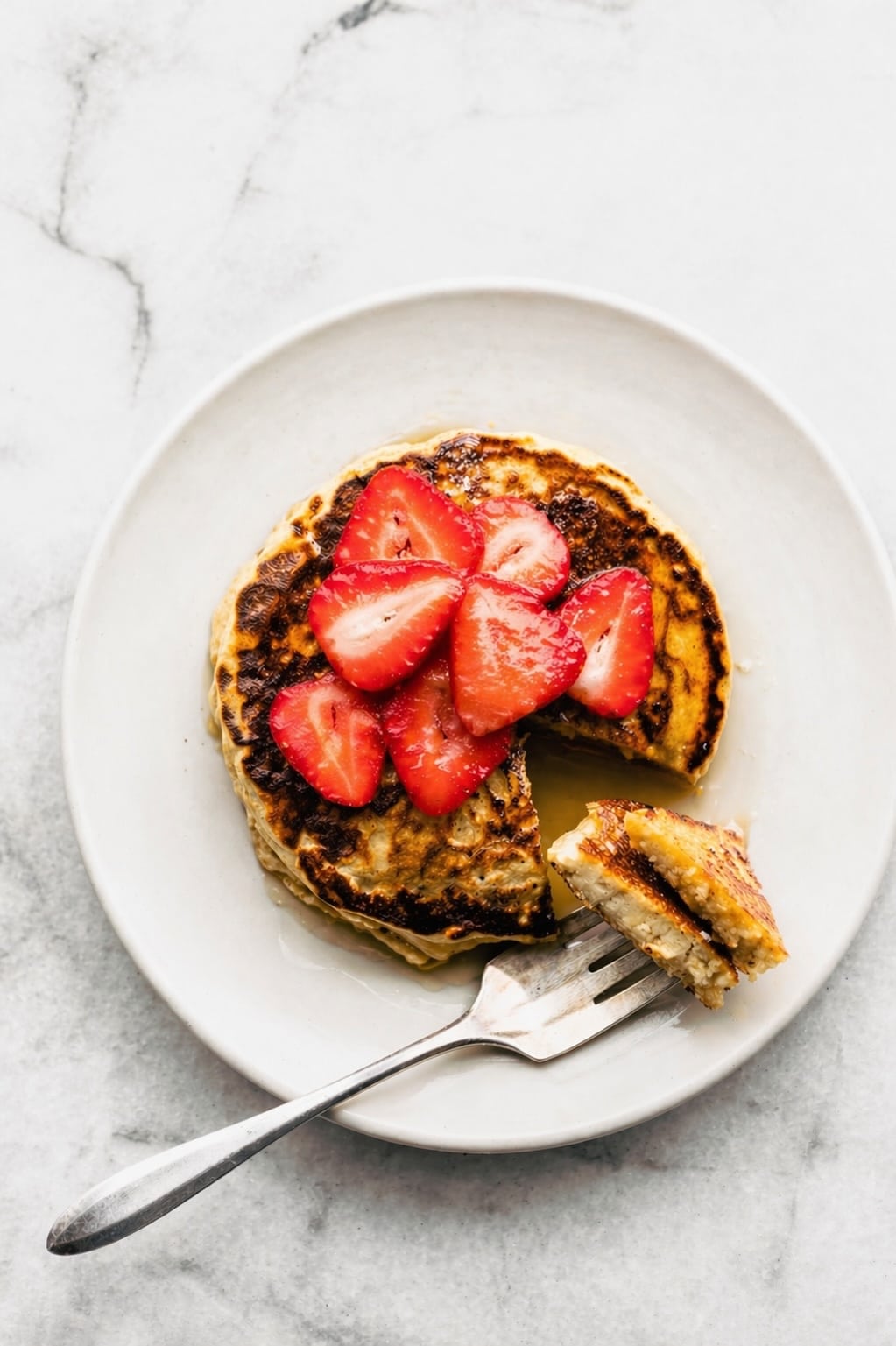 Gluten-free pancakes on a white plate topped with butter and syrup, with a fork holding a cut piece.