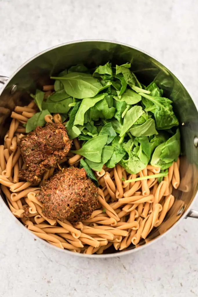 Large pot filled with pasta, spinach and sundried tomato pesto.