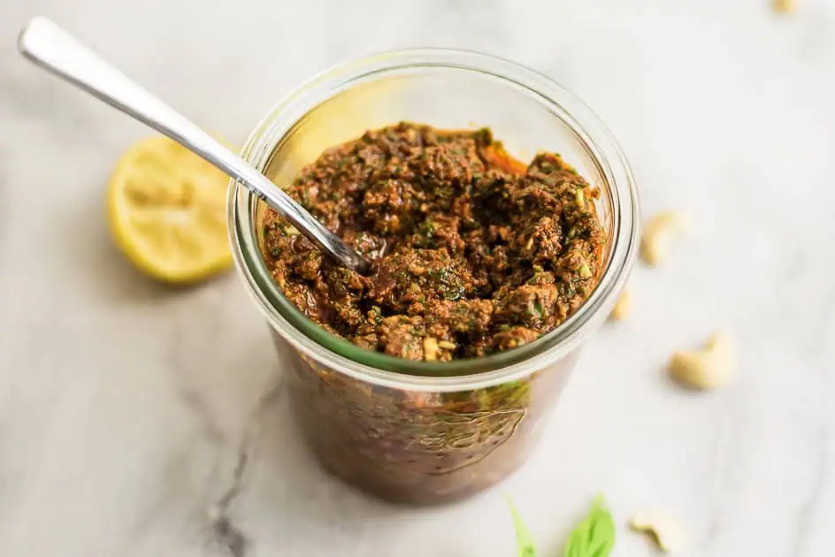 Spoon resting in a jar of sundried tomato pesto.