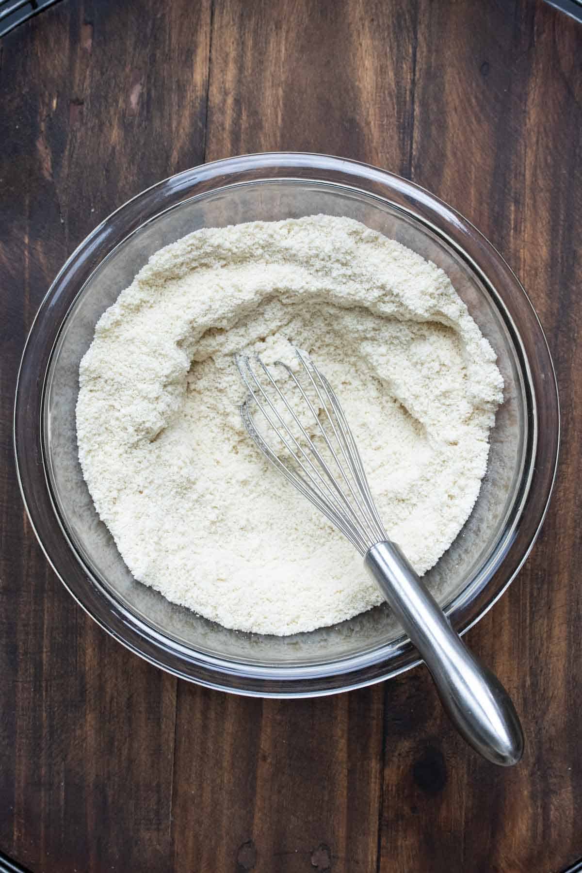 Glass bowl with flour being mixed with a whisk