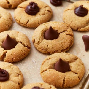 A tray of gluten-free peanut butter blossom cookies, featuring crackled golden edges and chocolate drops or swirls in the center, resting on parchment paper.