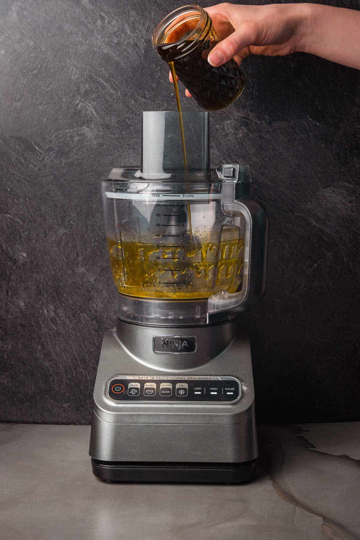 A person pouring a liquid into a food processor.