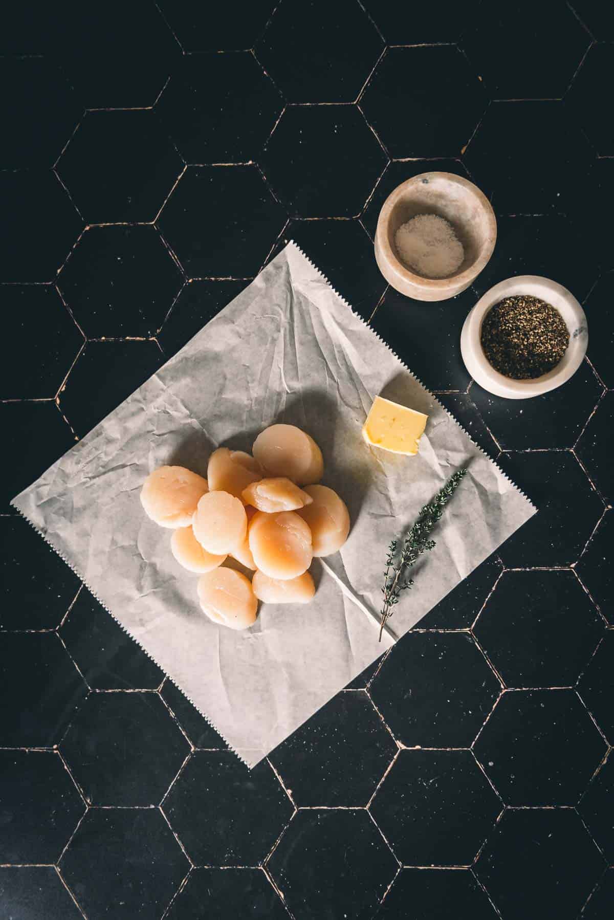 Sea Scallops on a piece of paper on a black table.