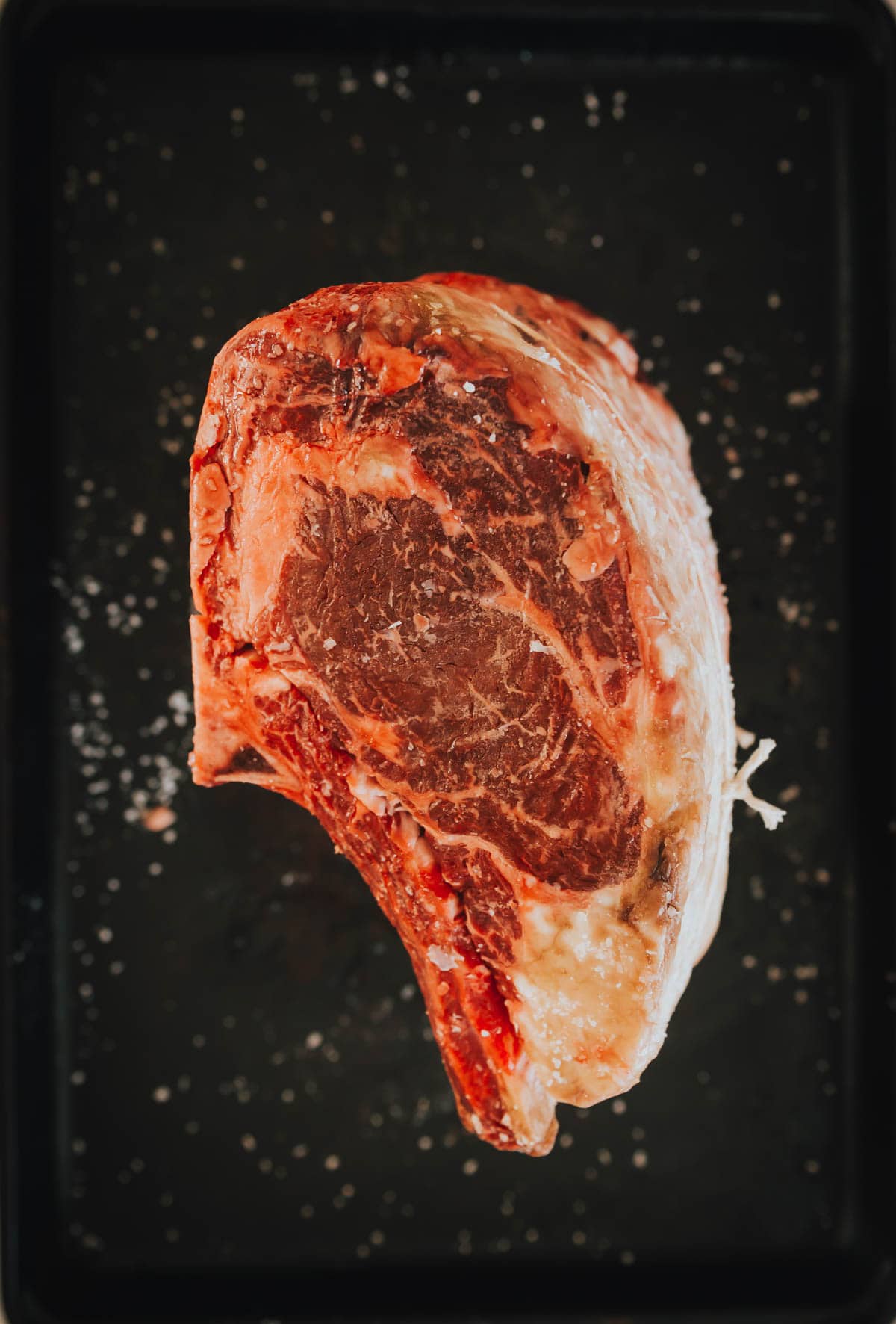 A standing rib roast on it's side to show the marbling on a black tray.