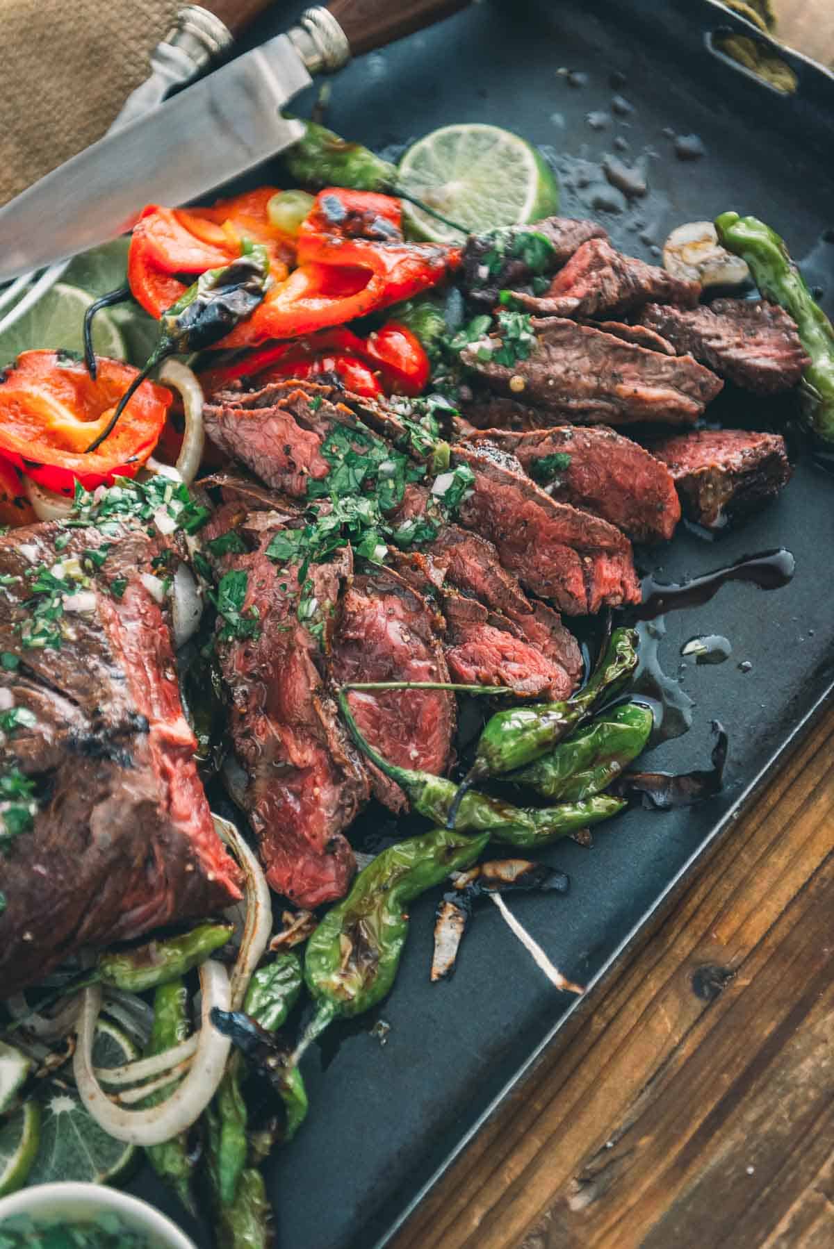 Grilled steak with peppers and onions on a black tray.