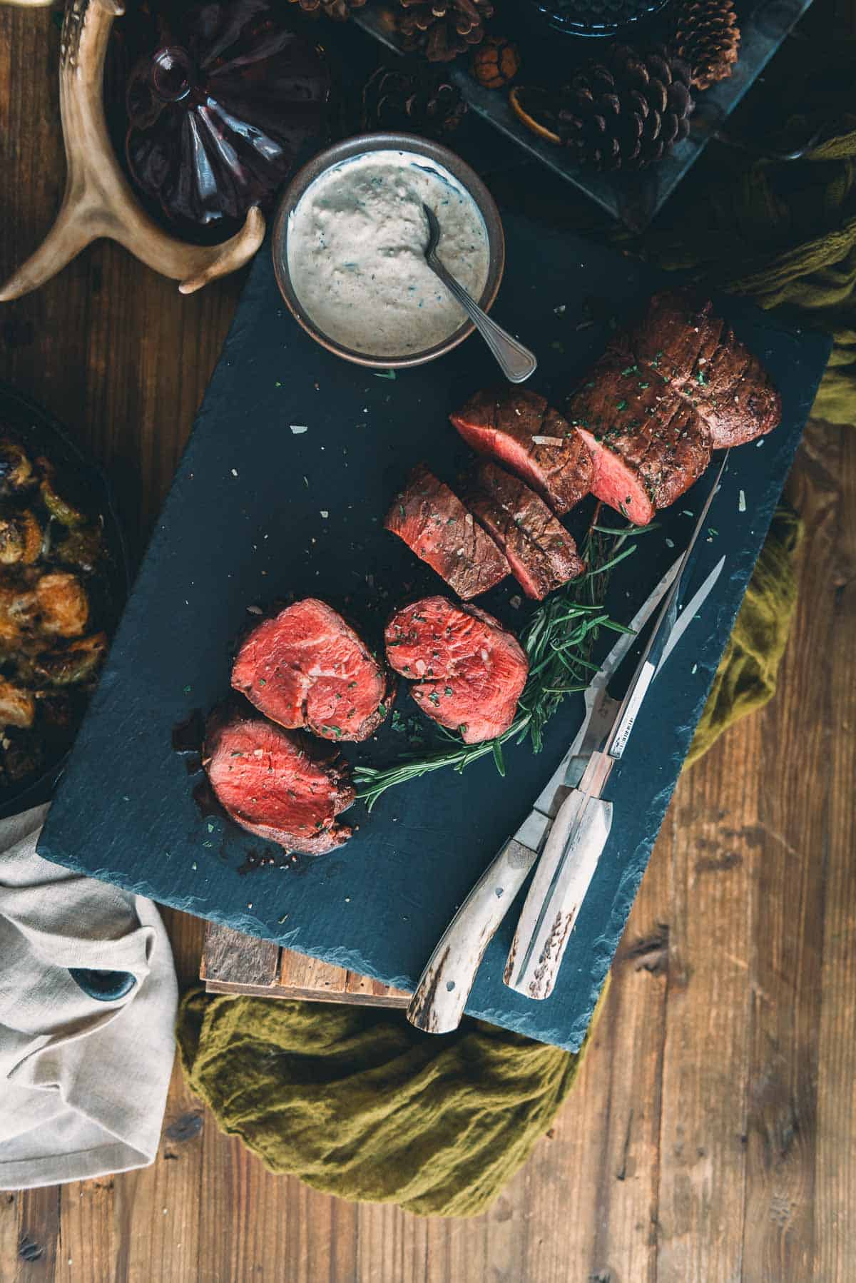 Sliced beef tenderloin on a black serving platter with sauce and herbs.