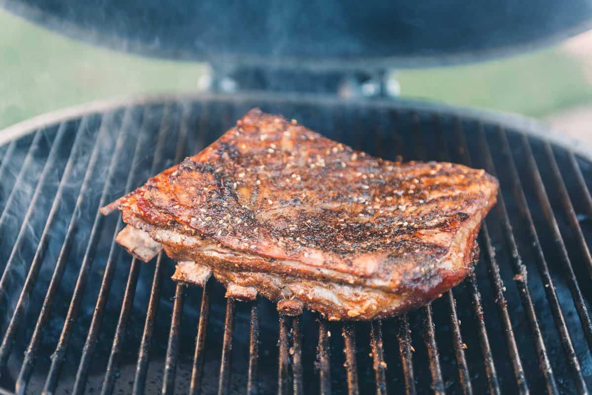 Lamb ribs flipped to sear the bone side of the rack on the barbecue grill.