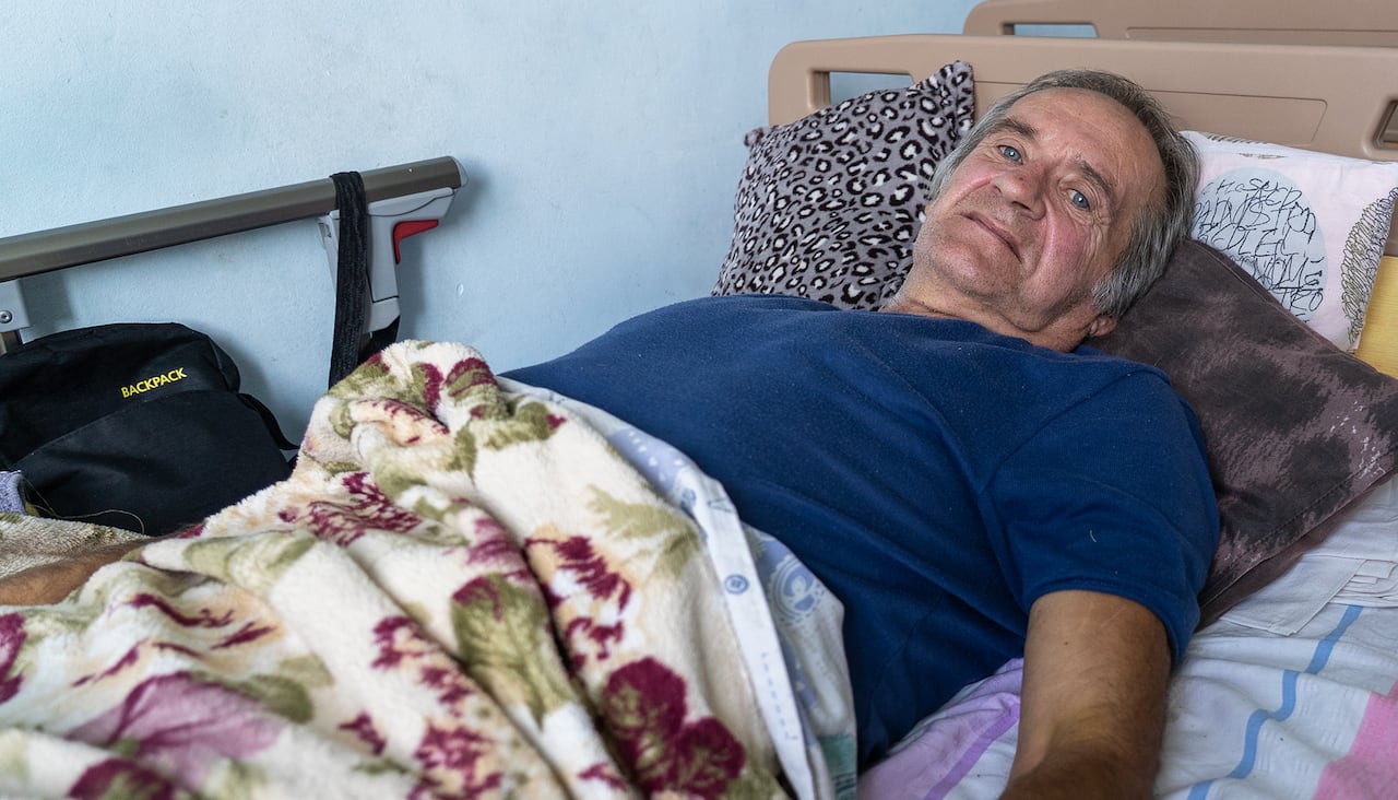 A grey-haired man lies in a bed.