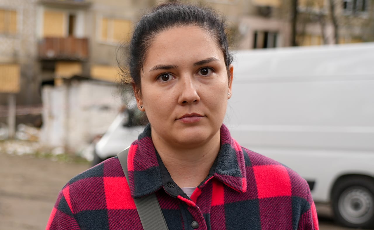 A woman in a checkered jacket looks at the camera.