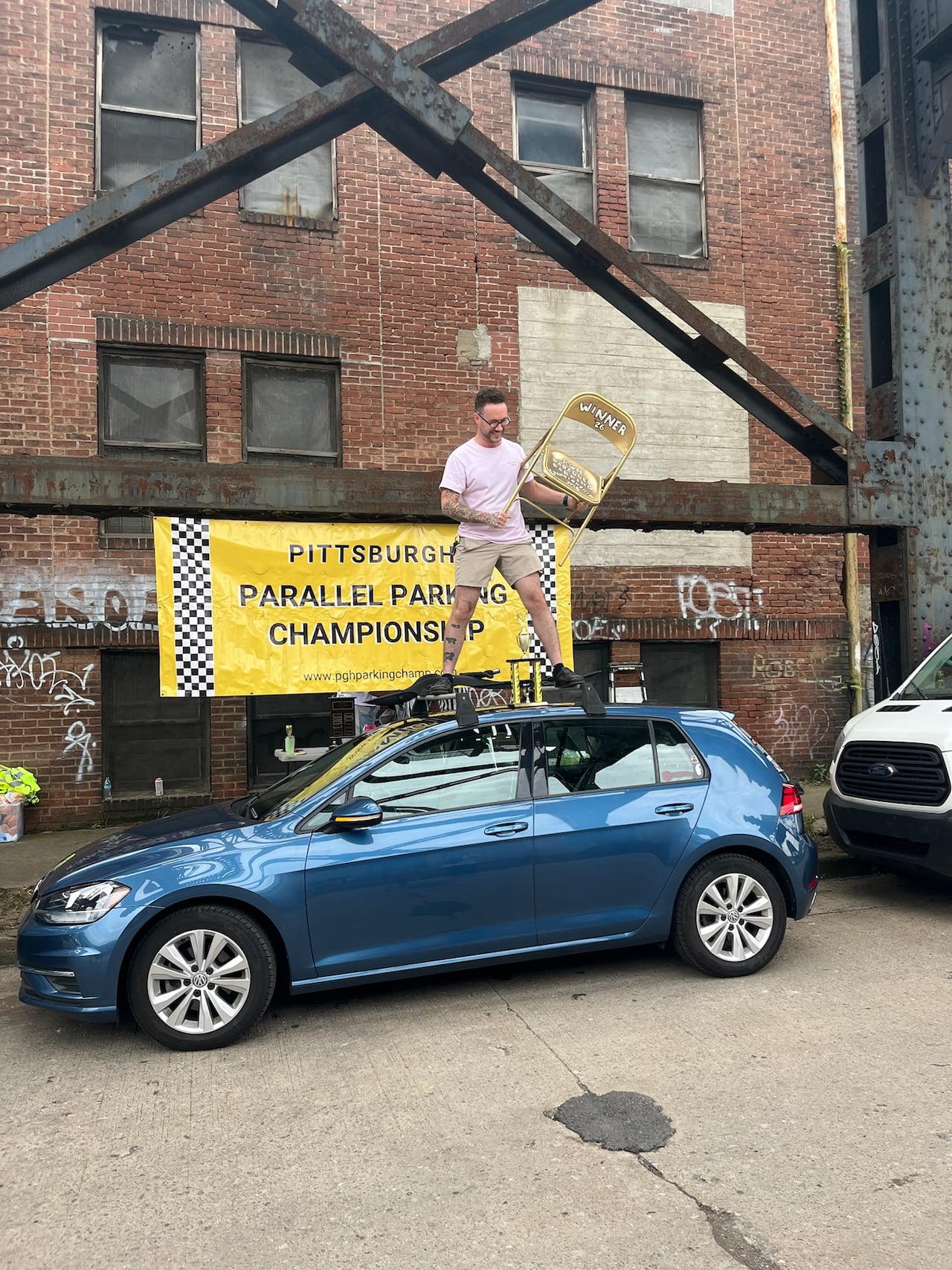 man standing on blue car holing silver chair