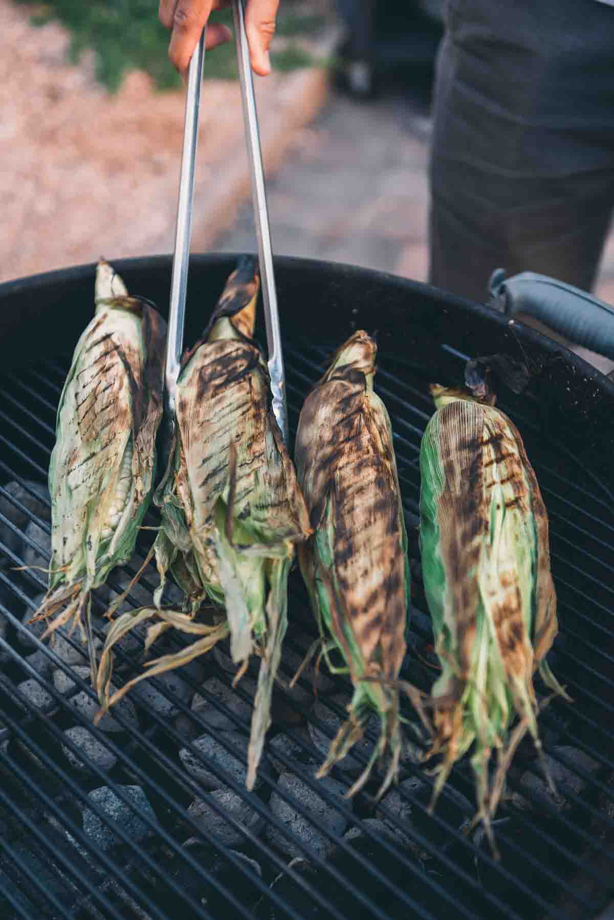 Tongs rotating corn to show charred sides.