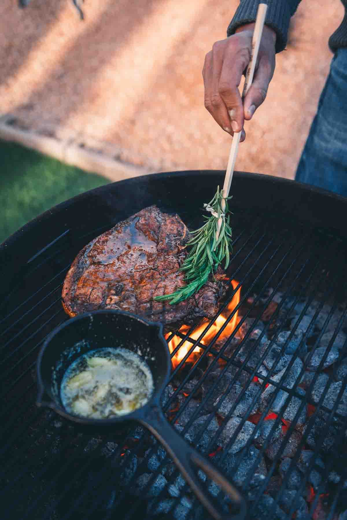 Porterhouse steak being brushed with herbs.