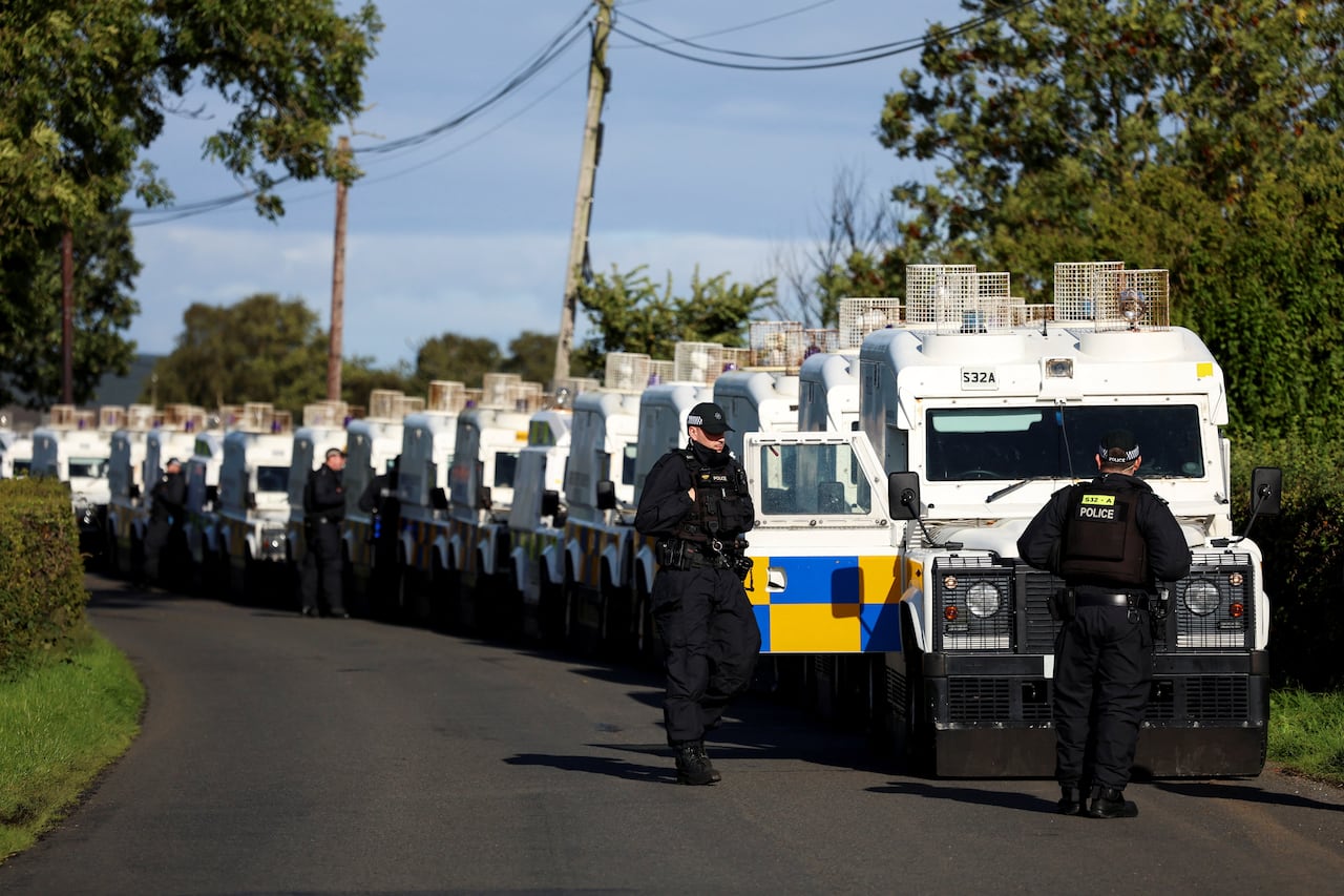 A line of armoured police vehicles is parked alongside a road.