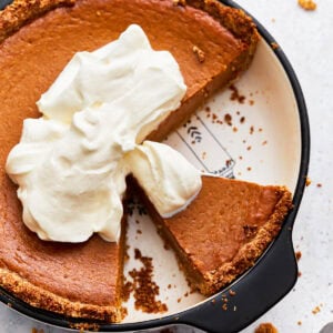 Overhead view of gluten-free pumpkin pie topped with whipped cream, in a pie dish with some slices missing.