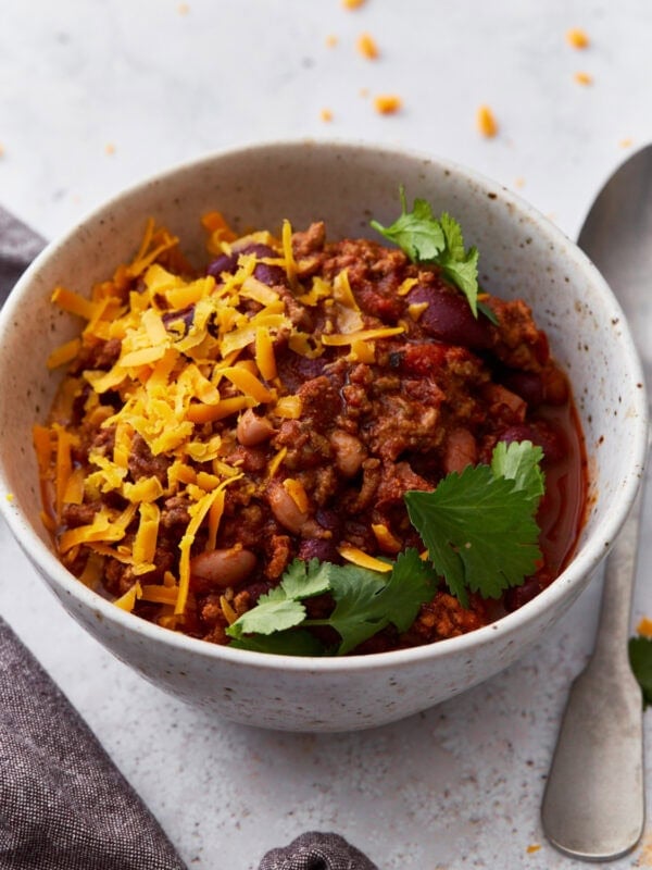 Closeup shot of a white bowl filled with gluten-free chili, topped with parsley and shredded orange cheese.