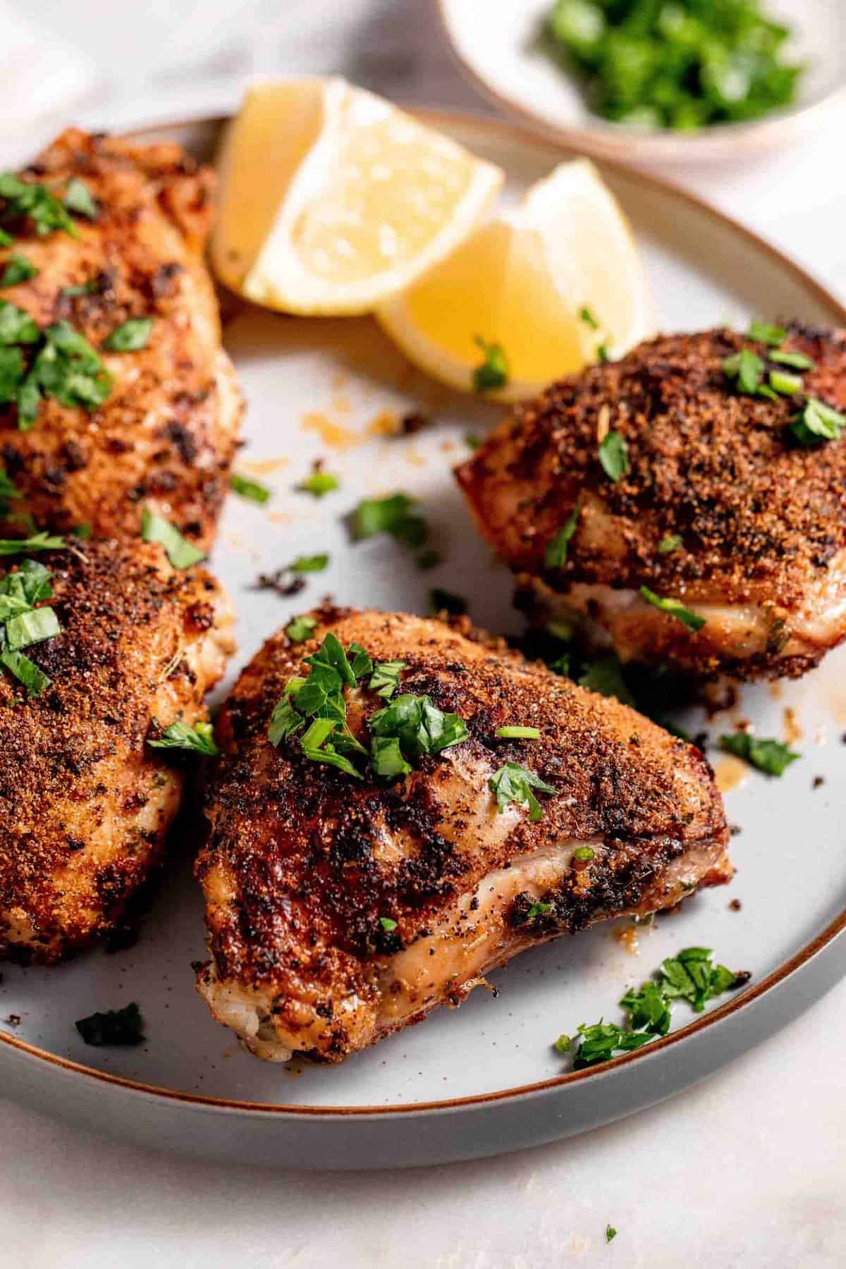Chicken thighs on a white platter garnished with lemons and minced parsley.