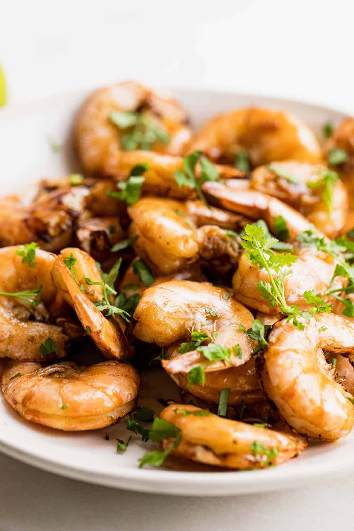 Close up of glistening cooked shrimp garnished with fresh parsley. 
