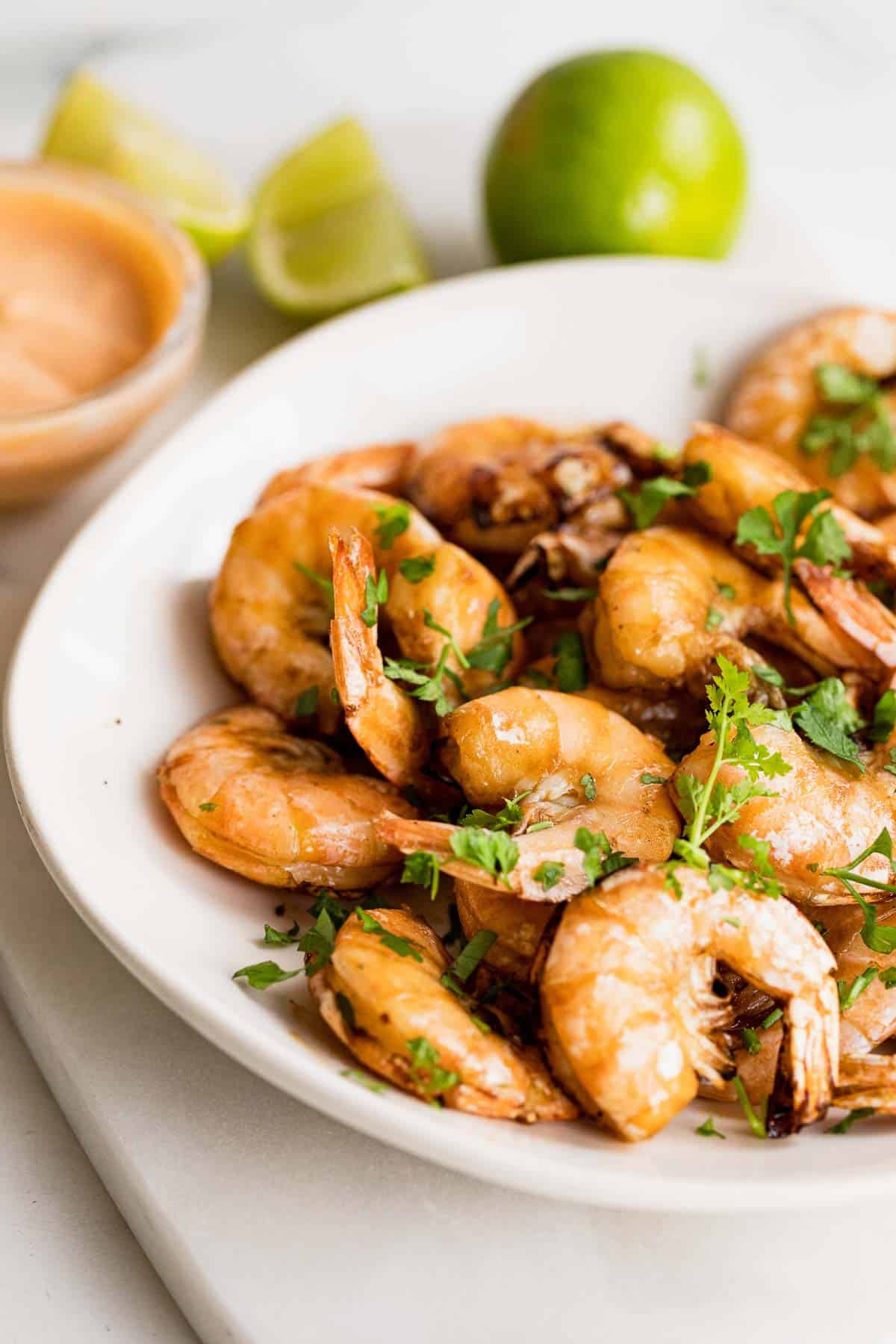White bowl filled with cooked shrimp with dipping sauce and lime in background for serving. 