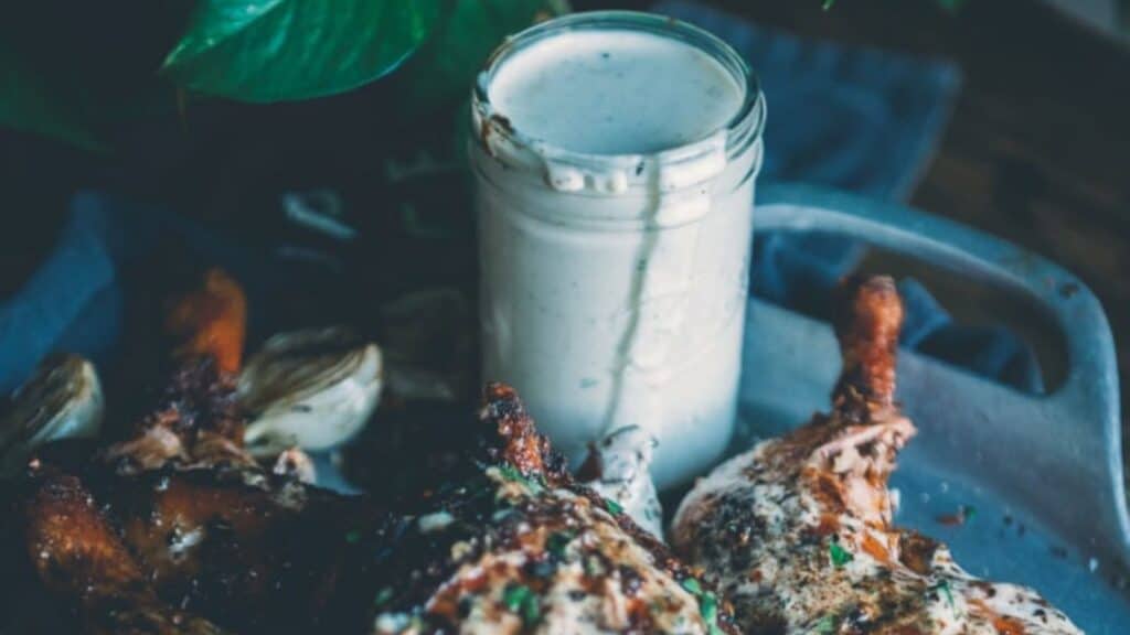 Jar of white BBQ sauce with pile of chicken. 