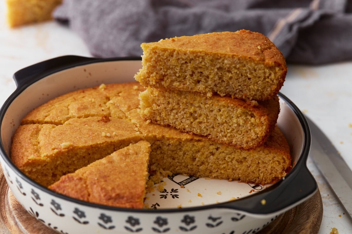 Two slices of almond flour cornbread stacked on top of the rest of the cornbread in a round baking dish.