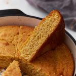 A wedge of almond flour cornbread propped up in a round baking dish, showing its moist, tender crumb.