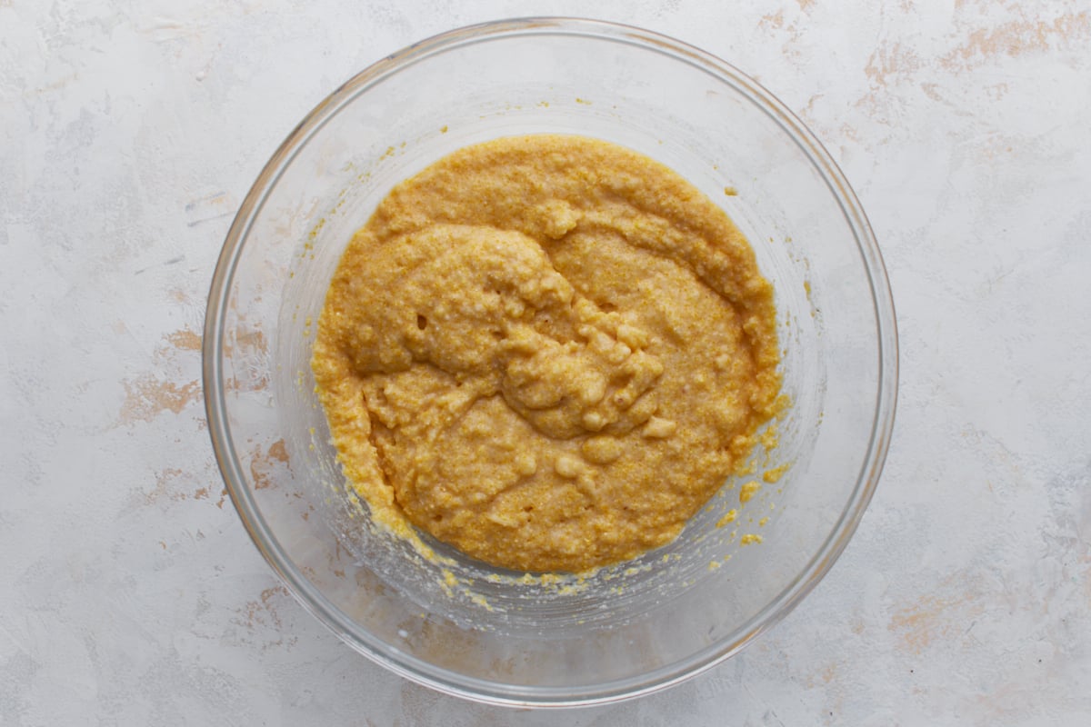 Thick almond flour cornbread batter mixed in a glass bowl after adding the egg, buttermilk, butter, and honey.
