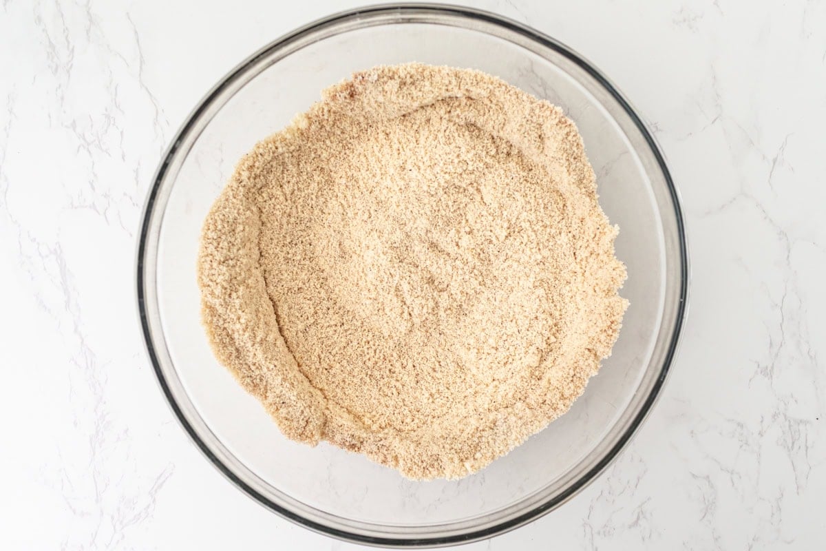 Almond flour and coconut flour whisked together with cinnamon, nutmeg, ginger, and cloves in a glass mixing bowl.