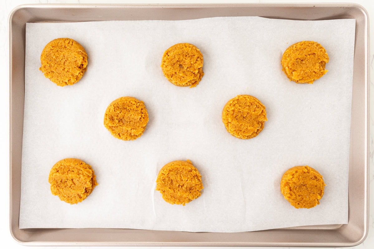 Scooped and flattened pumpkin cookie dough on a parchment-lined baking sheet before baking.