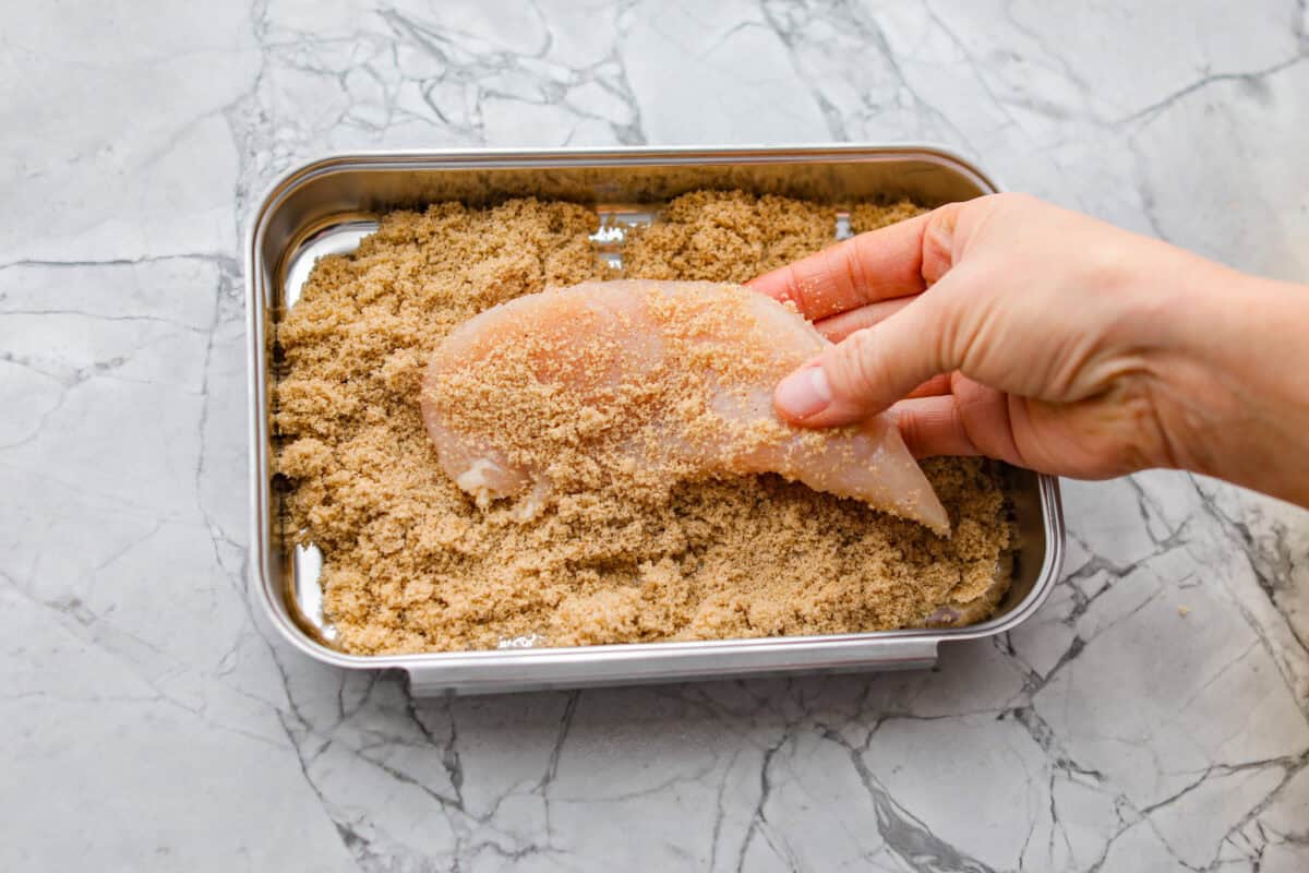Bacon brown sugar chicken tenders are sweet, smoky, and slightly spicy. Made with only a few simple ingredients, they're like candied bacon hugging juicy chicken without being overly sweet. Great as a main or appetizer, and always a total hit! Chicken tenders being coated with the brown sugar mixture.