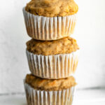 a stack of three freshly baked banana protein muffins in paper liners.
