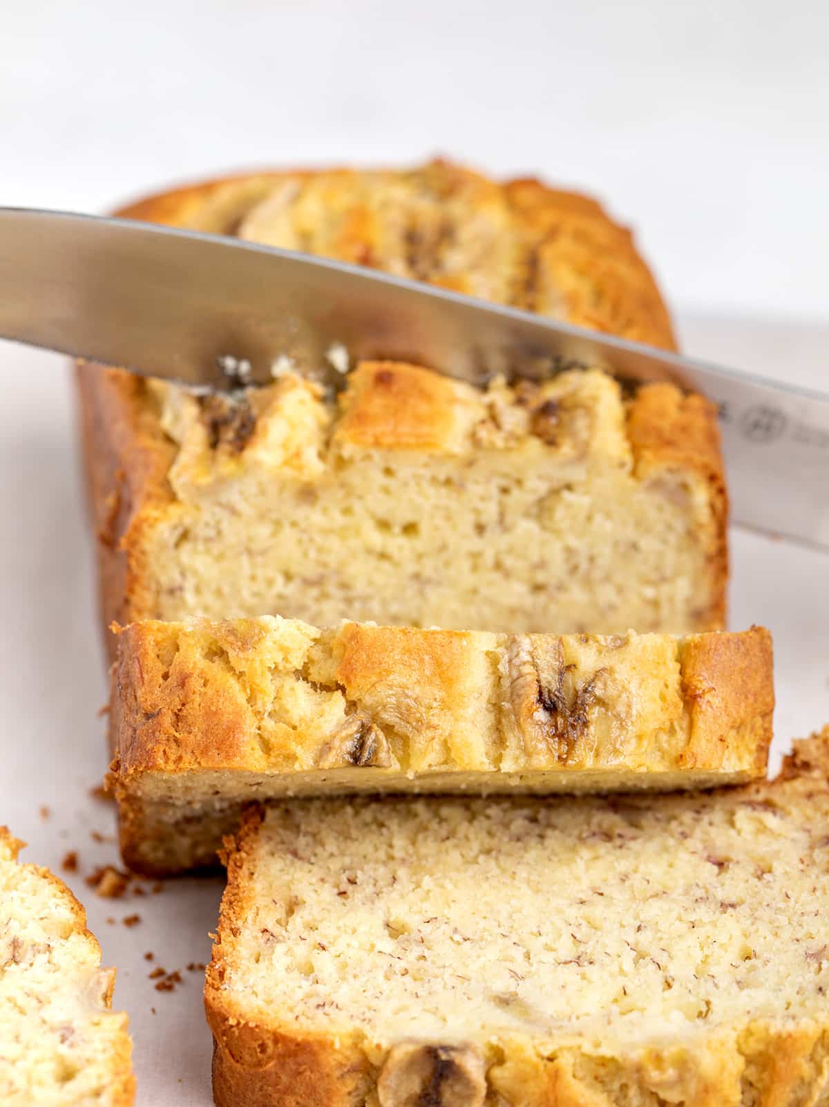 The GF banana bread with bananas on top being sliced with large knife.