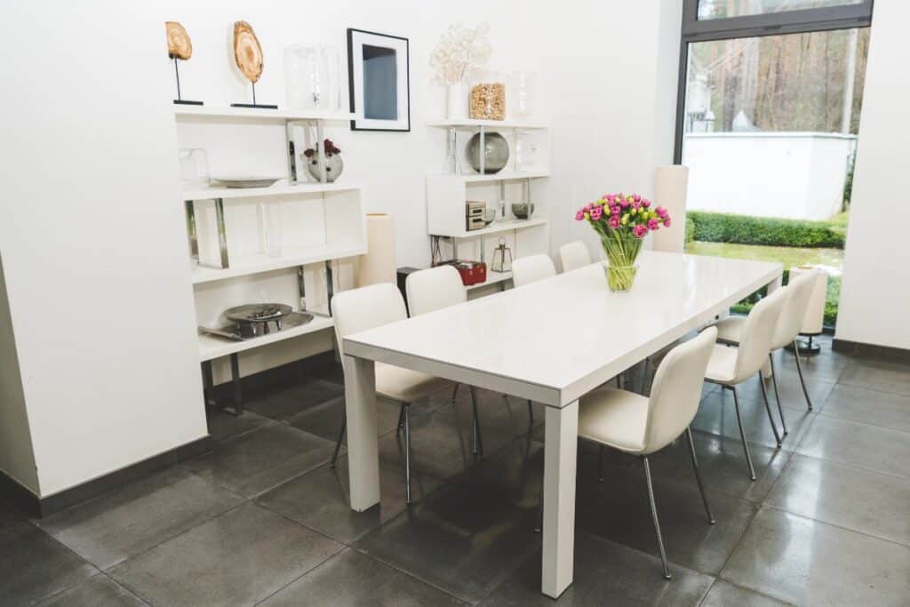 Bright modern dining room with white table, dining chairs and vase of flowers.