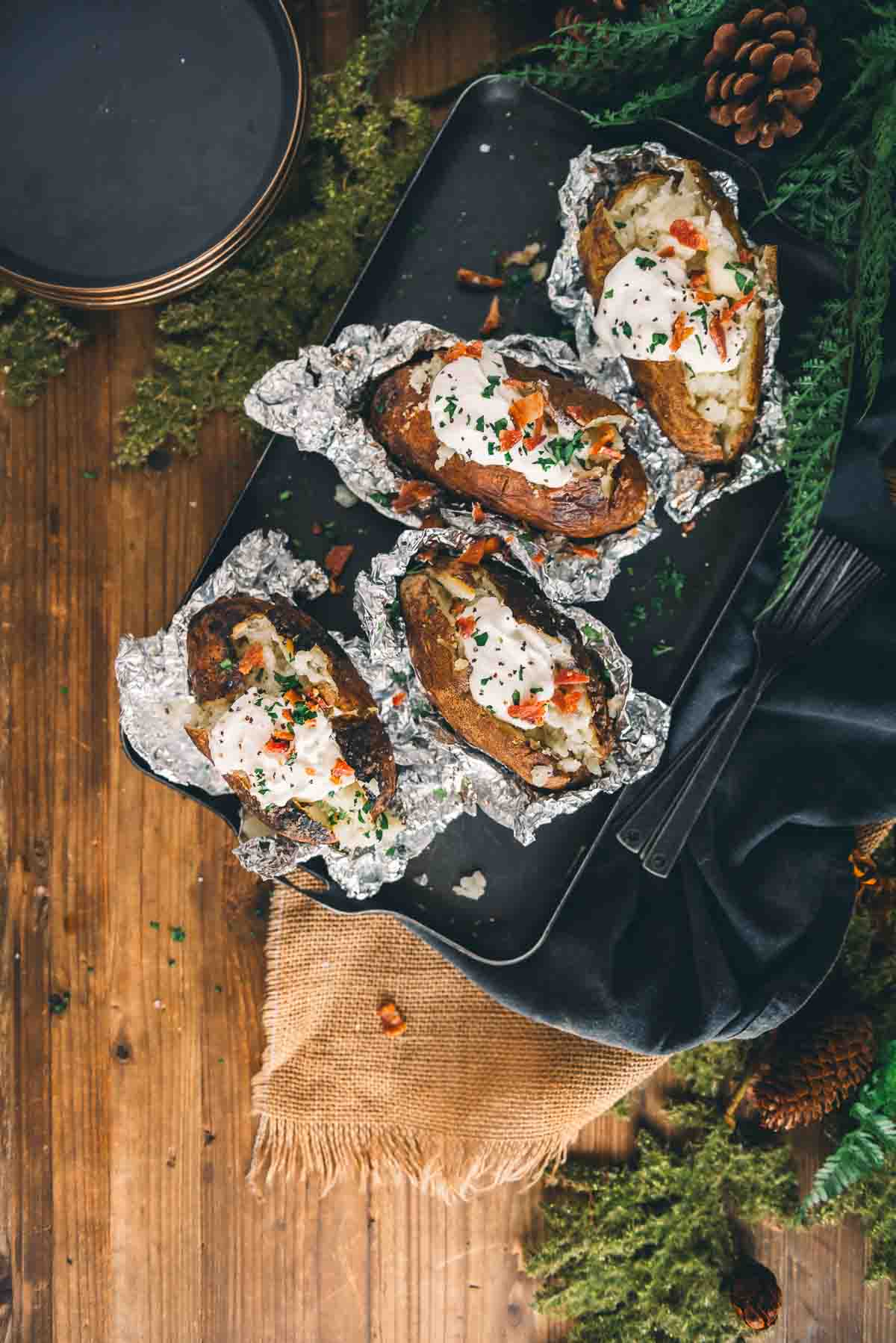 Overhead shot of baked potatoes opened from foil and topped with classic toppings. 
