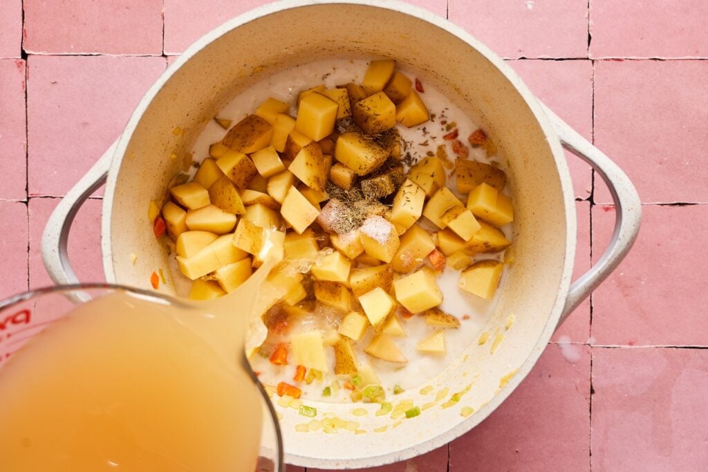 Adding potatoes and broth to the veggies in a dutch oven. 