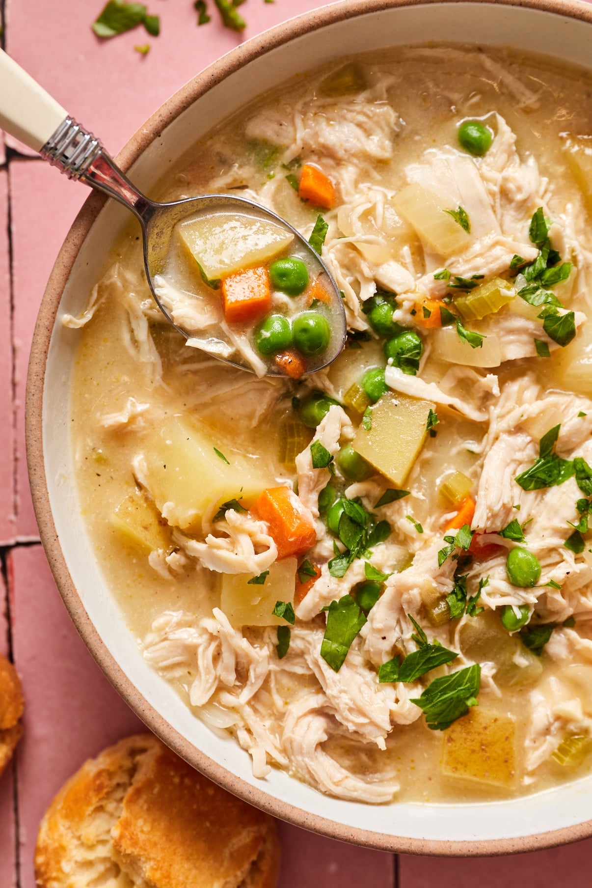 A spoon lifting a bite of chicken pot pie soup out of a bowl. 